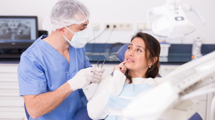 Woman in a dental chair holding her cheek in pain as a concerned dentist examines her.