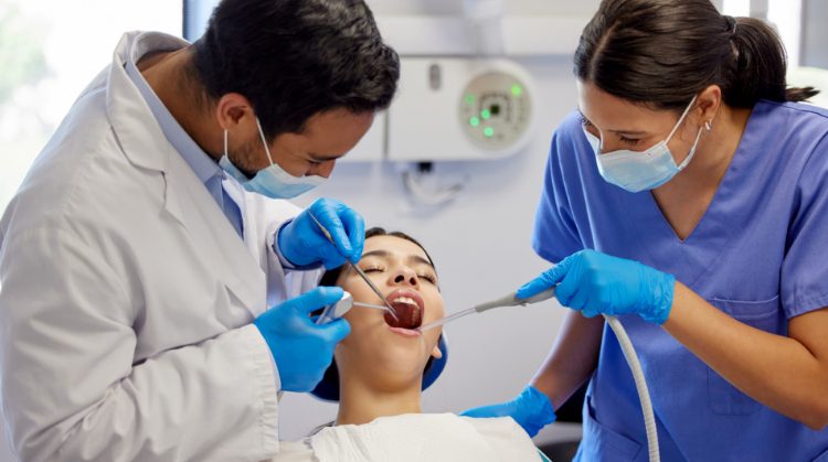 A dentist and assistant perform dental cleanings on a patient in a clinic.